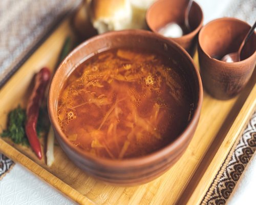 A comforting serving of clear traditional vegetable borscht inside a rustic ceramic bowl on a dark linen surface